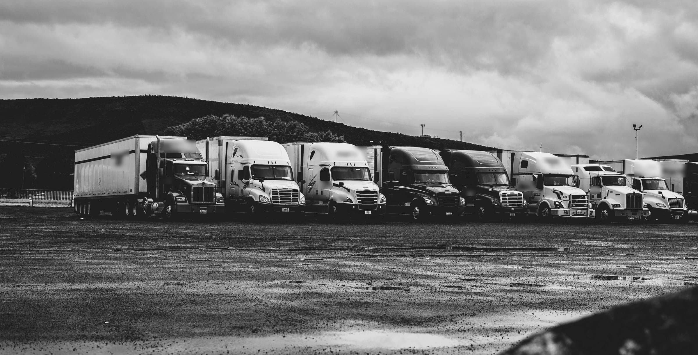 Black-and-white photo of semi-trucks with enclosed trailers lined up under a stormy sky