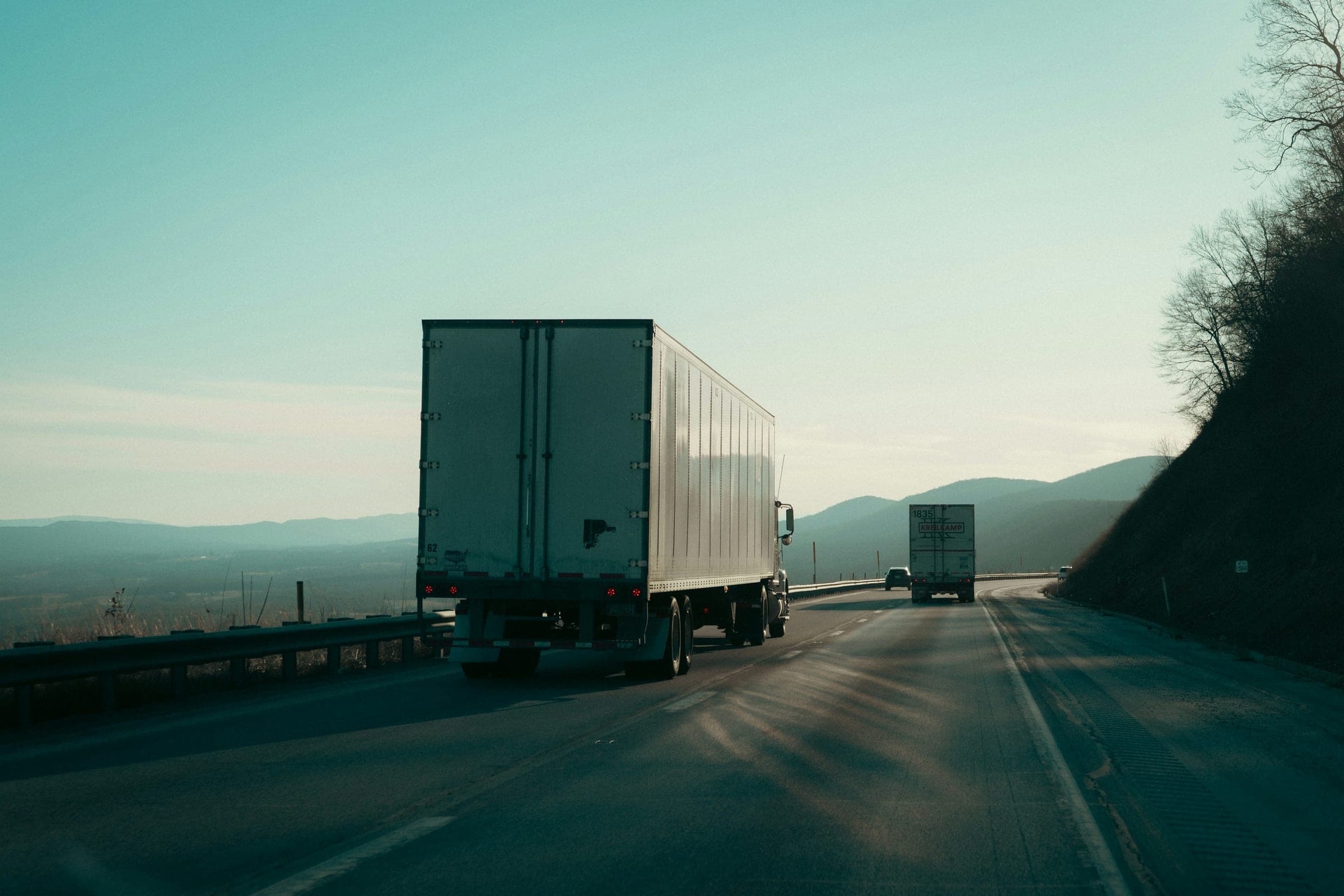 Enclosed dry van trailers heading down a mountain highway at dawn