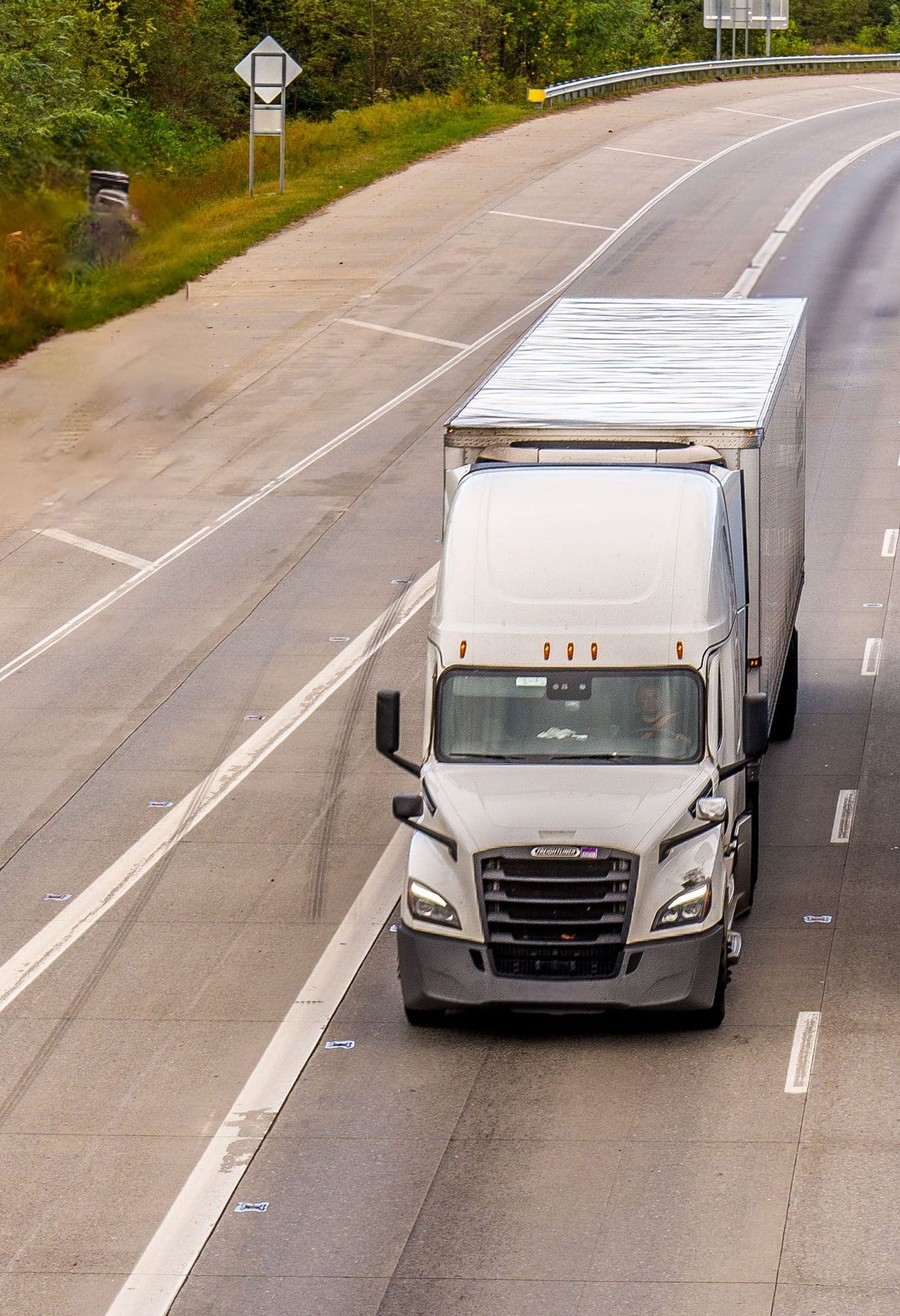 White Freightliner Cascadia pulling an enclosed dry van trailer on a divided highway