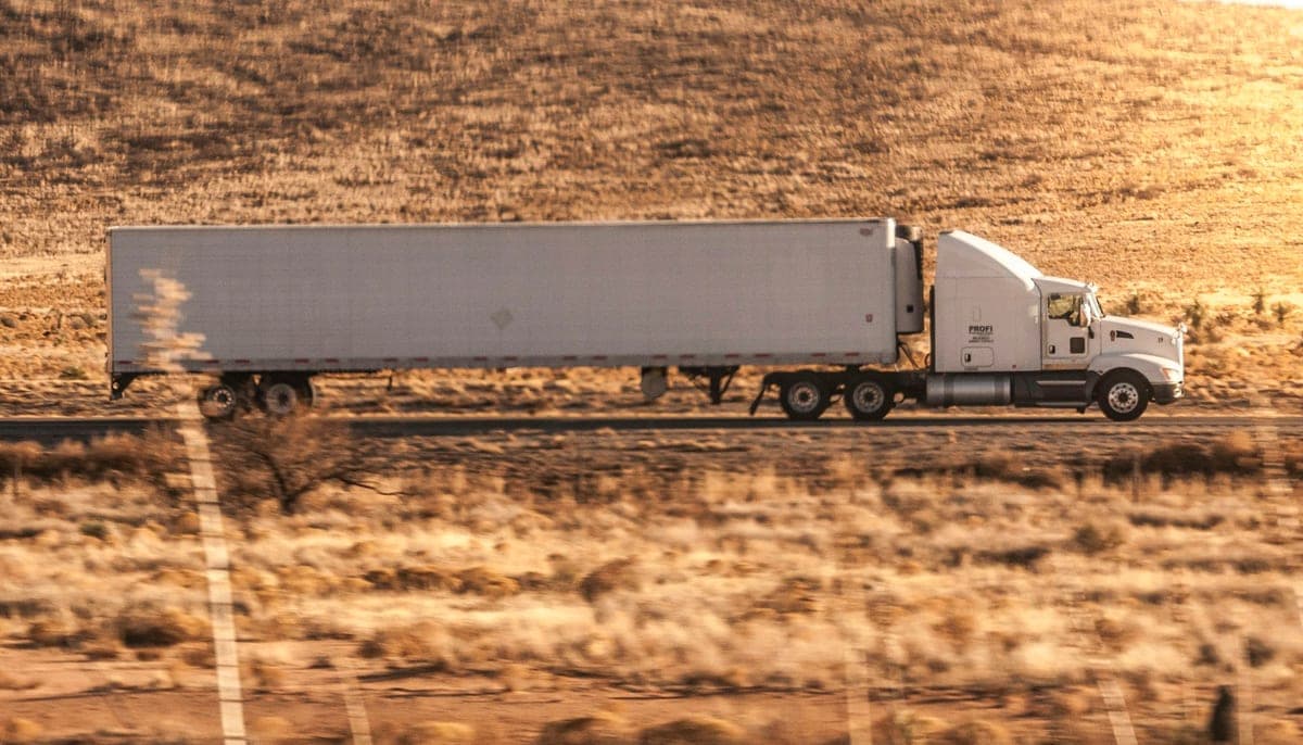 White semi-truck pulling an enclosed trailer across a sunlit desert